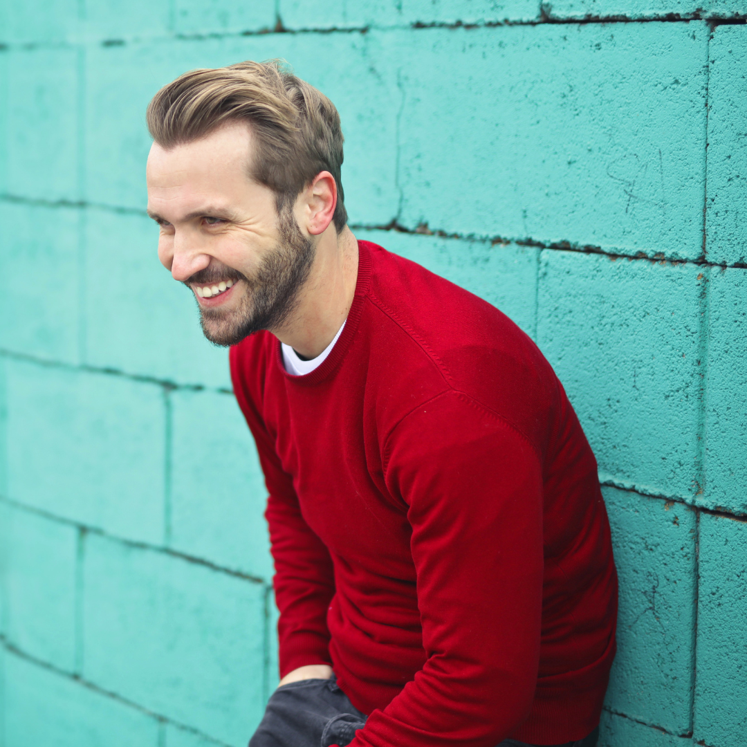 Happy man laughing in red shirt against turquoise wall